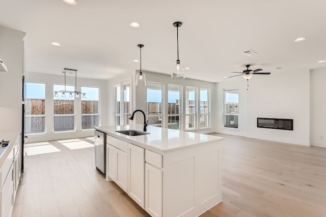 kitchen with a center island with sink, stainless steel dishwasher, pendant lighting, light hardwood / wood-style floors, and sink