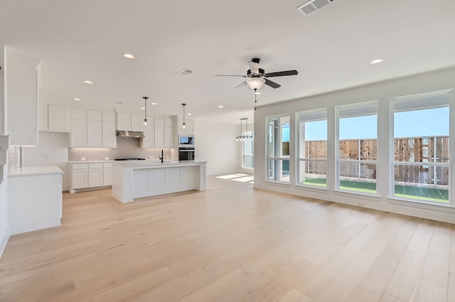 kitchen with white cabinets, an island with sink, light wood-type flooring, pendant lighting, and stainless steel appliances