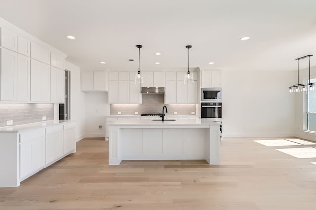 kitchen featuring white cabinetry, hanging light fixtures, stainless steel appliances, and a center island with sink