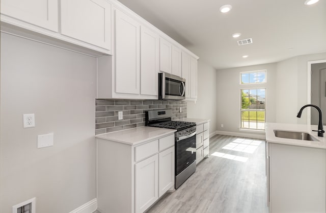 kitchen with sink, light hardwood / wood-style floors, tasteful backsplash, white cabinetry, and stainless steel appliances