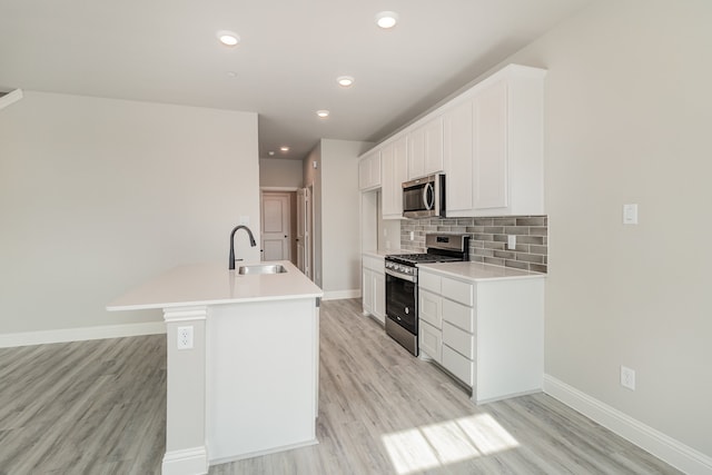 kitchen with stainless steel appliances, white cabinetry, a center island with sink, and light wood-type flooring