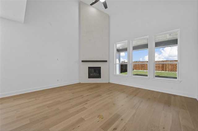 unfurnished living room with a high ceiling, a large fireplace, light hardwood / wood-style flooring, and ceiling fan