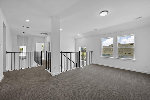 spare room featuring dark colored carpet, vaulted ceiling, and an inviting chandelier