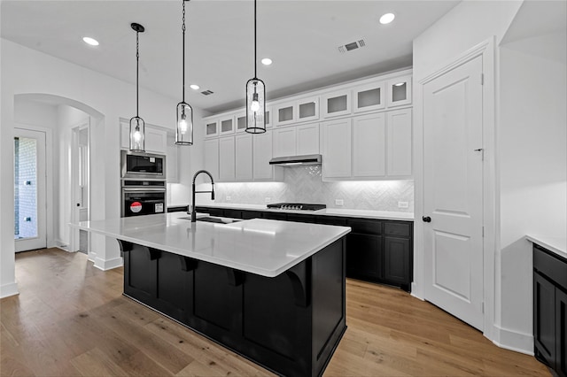 kitchen featuring stainless steel appliances, white cabinetry, light hardwood / wood-style floors, and an island with sink