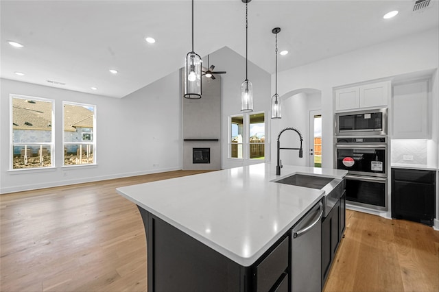 kitchen featuring stainless steel appliances, hanging light fixtures, tasteful backsplash, light hardwood / wood-style flooring, and an island with sink