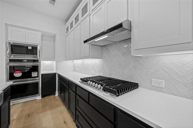 kitchen with white cabinets, appliances with stainless steel finishes, backsplash, and light hardwood / wood-style flooring