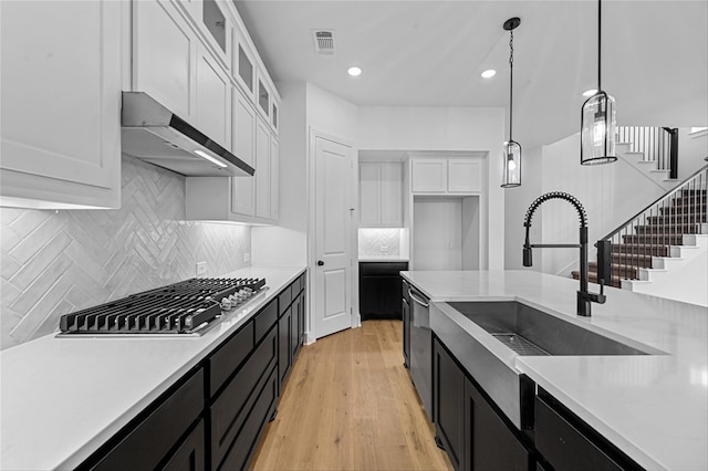 kitchen with appliances with stainless steel finishes, sink, decorative light fixtures, light hardwood / wood-style flooring, and white cabinets