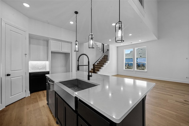 kitchen featuring dishwasher, sink, hanging light fixtures, light hardwood / wood-style flooring, and an island with sink