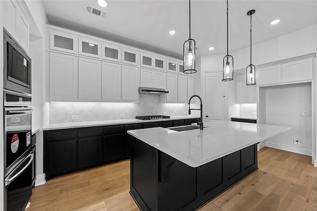 kitchen featuring light wood-type flooring, white cabinetry, sink, and an island with sink