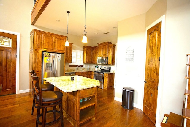 kitchen featuring sink, hanging light fixtures, stainless steel appliances, light stone counters, and a kitchen island