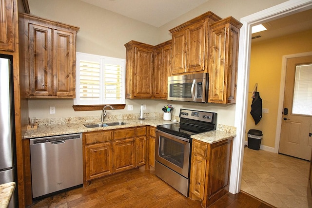 kitchen featuring stainless steel appliances, dark hardwood / wood-style flooring, light stone countertops, and sink