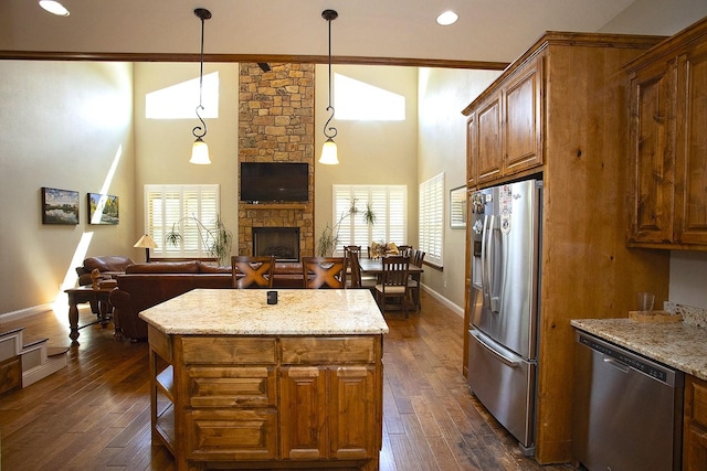 kitchen featuring pendant lighting, dark wood-type flooring, stainless steel appliances, a fireplace, and light stone countertops