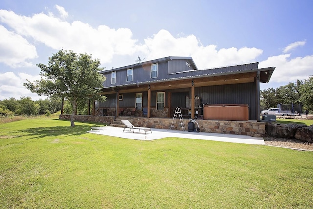 rear view of house featuring a hot tub, a patio, and a lawn