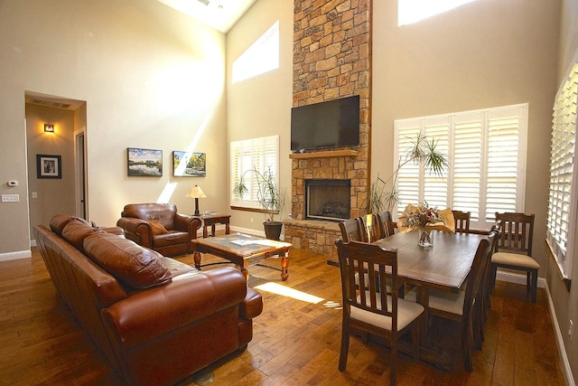 living room with a stone fireplace, wood-type flooring, and a towering ceiling