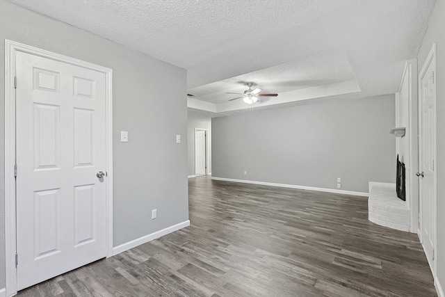 unfurnished living room with a textured ceiling, a raised ceiling, ceiling fan, and dark wood-type flooring