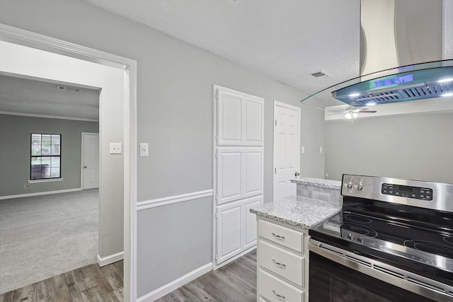 kitchen with light stone counters, electric stove, range hood, white cabinetry, and dark carpet