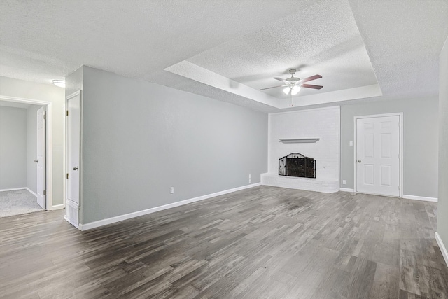 unfurnished living room with hardwood / wood-style floors, a fireplace, a raised ceiling, and ceiling fan