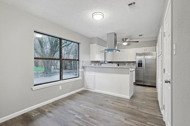 kitchen featuring wood-type flooring, island range hood, kitchen peninsula, tasteful backsplash, and stainless steel fridge