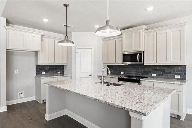 kitchen with decorative backsplash, light stone counters, a kitchen island with sink, and decorative light fixtures