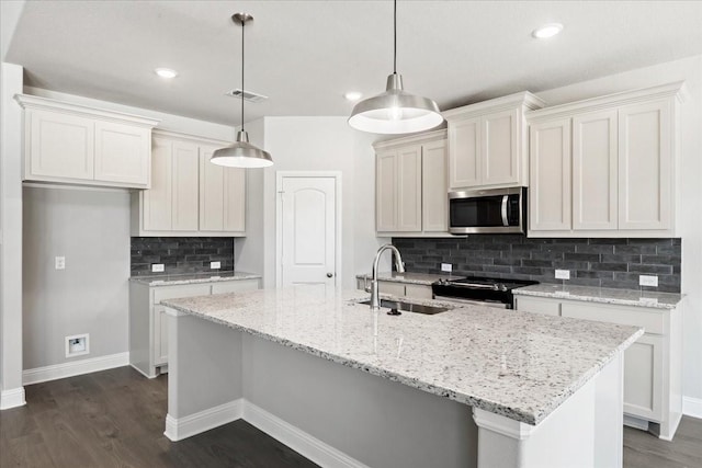 kitchen with hanging light fixtures, stainless steel appliances, a center island with sink, and sink