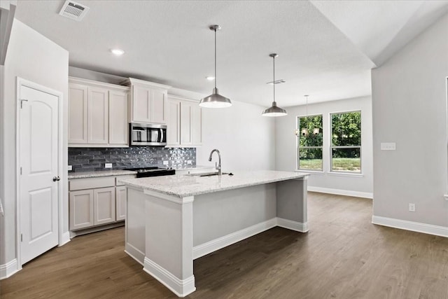 kitchen with white cabinetry, sink, hanging light fixtures, and an island with sink