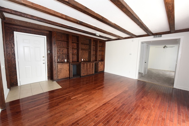 unfurnished living room featuring beam ceiling, carpet, and built in shelves