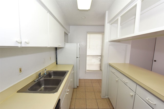 kitchen featuring light tile flooring, a textured ceiling, white cabinetry, sink, and white refrigerator