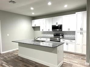 kitchen with a kitchen island with sink, range, white cabinetry, hardwood / wood-style floors, and tasteful backsplash