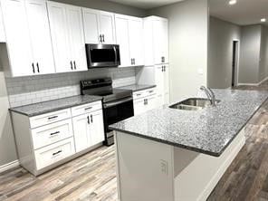 kitchen featuring electric range oven, tasteful backsplash, hardwood / wood-style flooring, white cabinetry, and sink