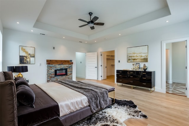 bedroom featuring ensuite bath, ceiling fan, light wood-type flooring, and a tray ceiling