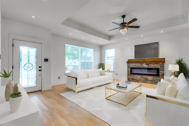 living room featuring ceiling fan, a raised ceiling, a fireplace, and light hardwood / wood-style flooring