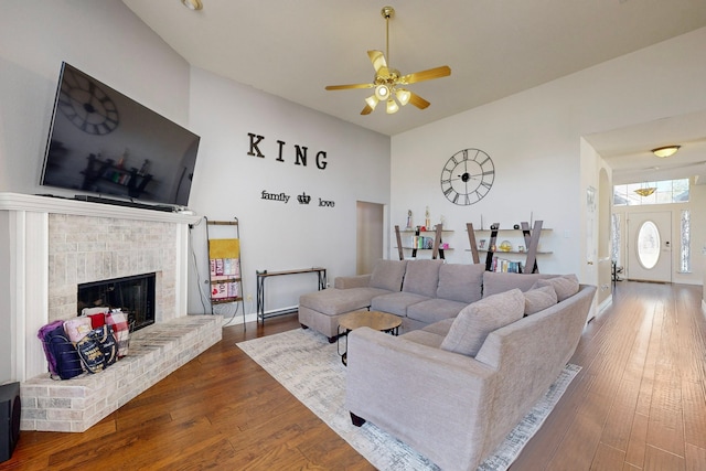 living room with a brick fireplace, dark hardwood / wood-style floors, and ceiling fan