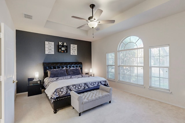 bedroom with light colored carpet, a raised ceiling, and ceiling fan