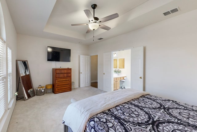 bedroom featuring ceiling fan, light carpet, ensuite bathroom, and a raised ceiling