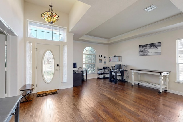 entrance foyer featuring ornamental molding, a raised ceiling, a notable chandelier, and dark hardwood / wood-style flooring