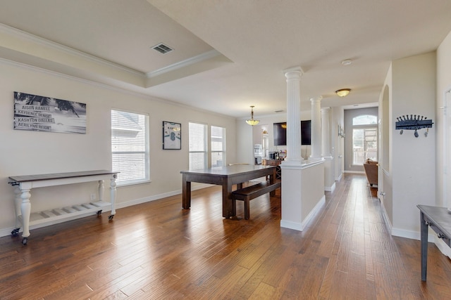 interior space featuring a raised ceiling, ornate columns, hardwood / wood-style flooring, ornamental molding, and an inviting chandelier