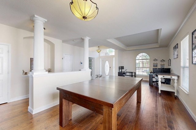 dining space with a raised ceiling, decorative columns, and hardwood / wood-style floors