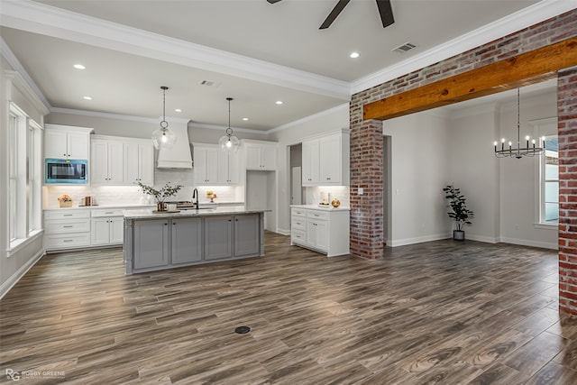 kitchen with white cabinets, dark hardwood / wood-style floors, a kitchen island with sink, and stainless steel microwave