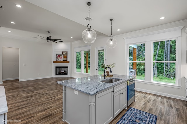 kitchen featuring light stone counters, dark hardwood / wood-style flooring, pendant lighting, sink, and stainless steel dishwasher