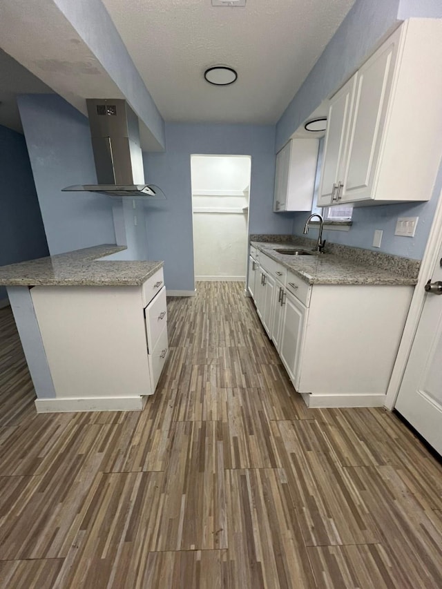 kitchen featuring sink, white cabinetry, hardwood / wood-style flooring, light stone countertops, and wall chimney range hood