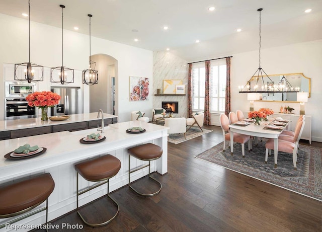 kitchen featuring dark wood-type flooring, a high end fireplace, pendant lighting, a breakfast bar area, and appliances with stainless steel finishes