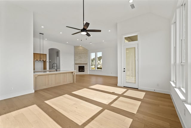 unfurnished living room featuring vaulted ceiling, a fireplace, sink, light hardwood / wood-style flooring, and ceiling fan