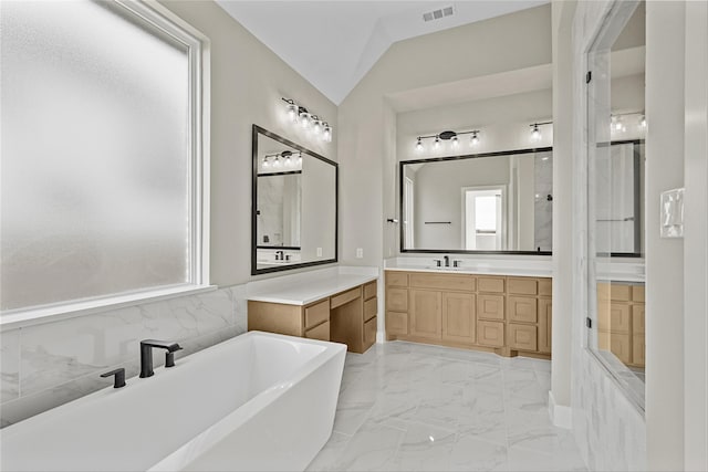 bathroom featuring a washtub, vanity, vaulted ceiling, and a healthy amount of sunlight