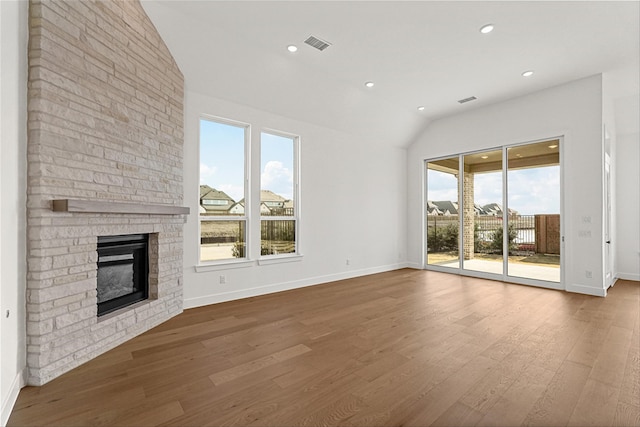 unfurnished living room featuring a brick fireplace, plenty of natural light, wood-type flooring, and lofted ceiling