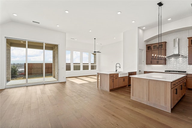 kitchen with wall chimney range hood, sink, pendant lighting, backsplash, and an island with sink