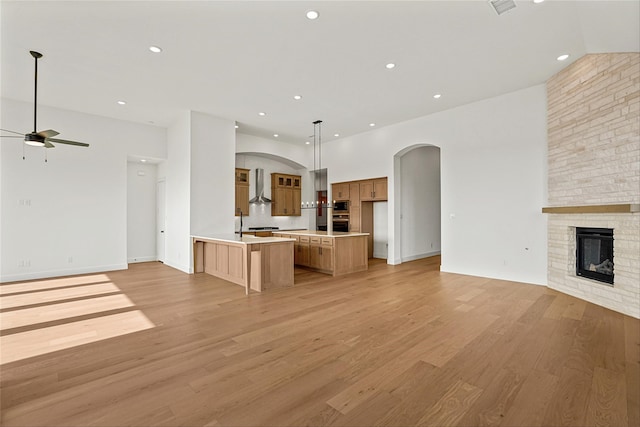 unfurnished living room with ceiling fan, a high ceiling, a stone fireplace, and light hardwood / wood-style floors