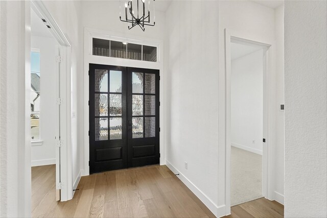 foyer featuring an inviting chandelier, french doors, and light wood-type flooring