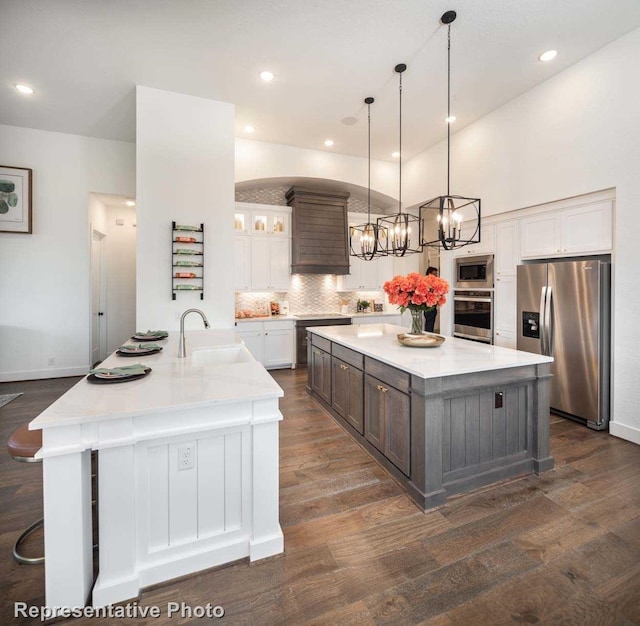 kitchen featuring a large island with sink, sink, stainless steel appliances, and dark wood-type flooring