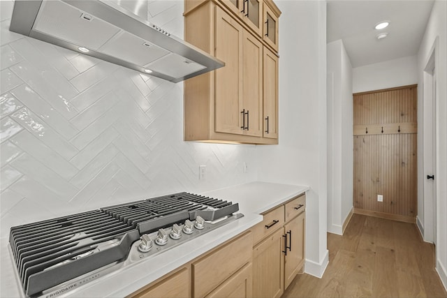 kitchen featuring wall chimney exhaust hood, light brown cabinets, light hardwood / wood-style floors, backsplash, and stainless steel gas stovetop