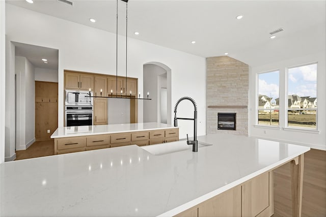 kitchen featuring a spacious island, pendant lighting, appliances with stainless steel finishes, a stone fireplace, and sink